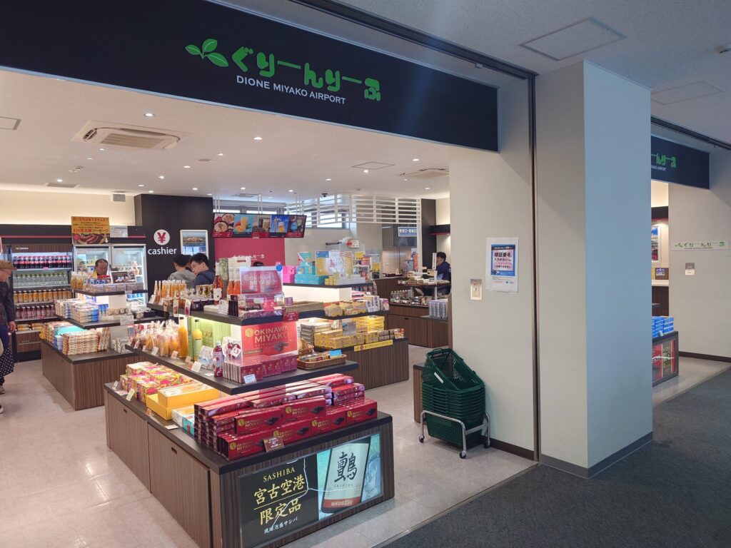 宮古空港の保安検査場通過後（エアサイド）にある売店「ぐりーんりーふ」の店舗正面。黒い看板に緑色で店名が書かれており、店内には宮古島限定の泡盛「サシバ」や沖縄土産のボックスが綺麗に陳列されている。