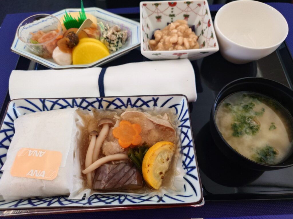 ANA812便ビジネスクラスで提供された和食。白身魚の西京焼き、煮物の小鉢、俵型のご飯、お味噌汁が陶器の器に並んでいる写真