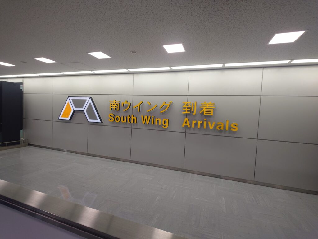 成田空港第1ターミナル南ウイング到着ロビーにある、「南ウイング 到着 South Wing Arrivals」と書かれた日本語と英語のサインの写真